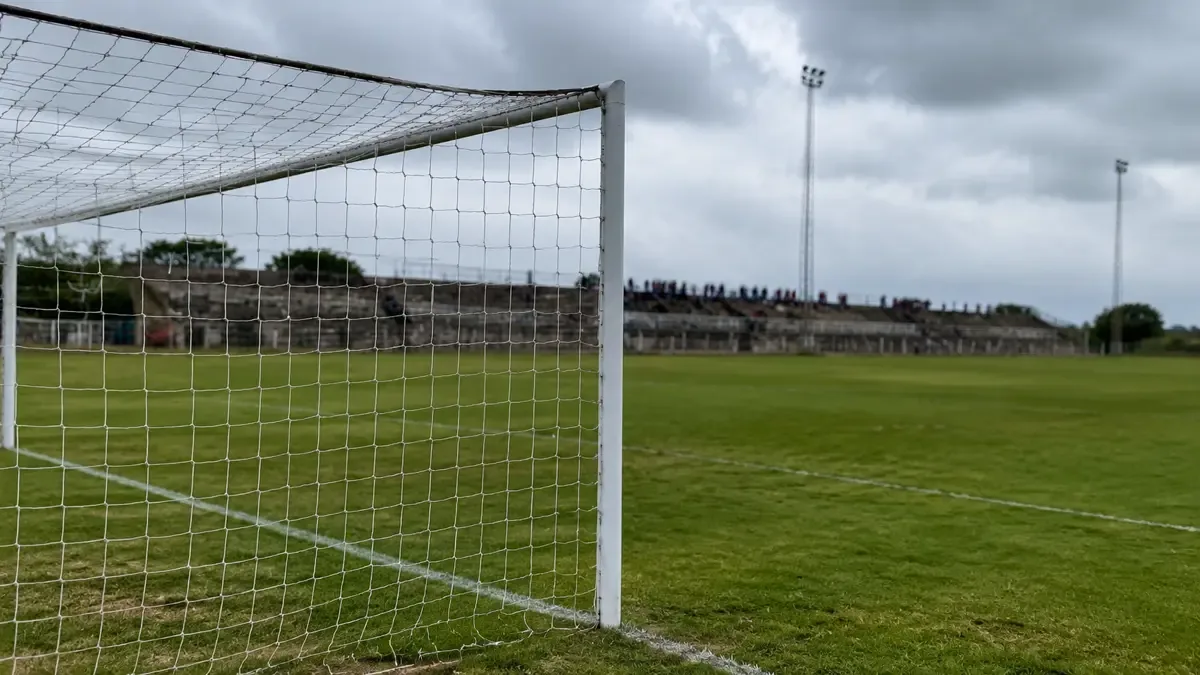 Estadio de fútbol de ascenso con tribuna de cemento en una tarde de partido
